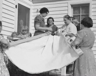 Farm women, members of the "Helping Hand" club,  carefully roll up the quilt upon which they are working 1939 Photo by Dorothea Lange Library of Congress Prints & Photographs Division  Farm Security Administration Office of War Information Washington, D.C. Item number LC-DIG-fsa-8b34965 www.loc.gov/pictures